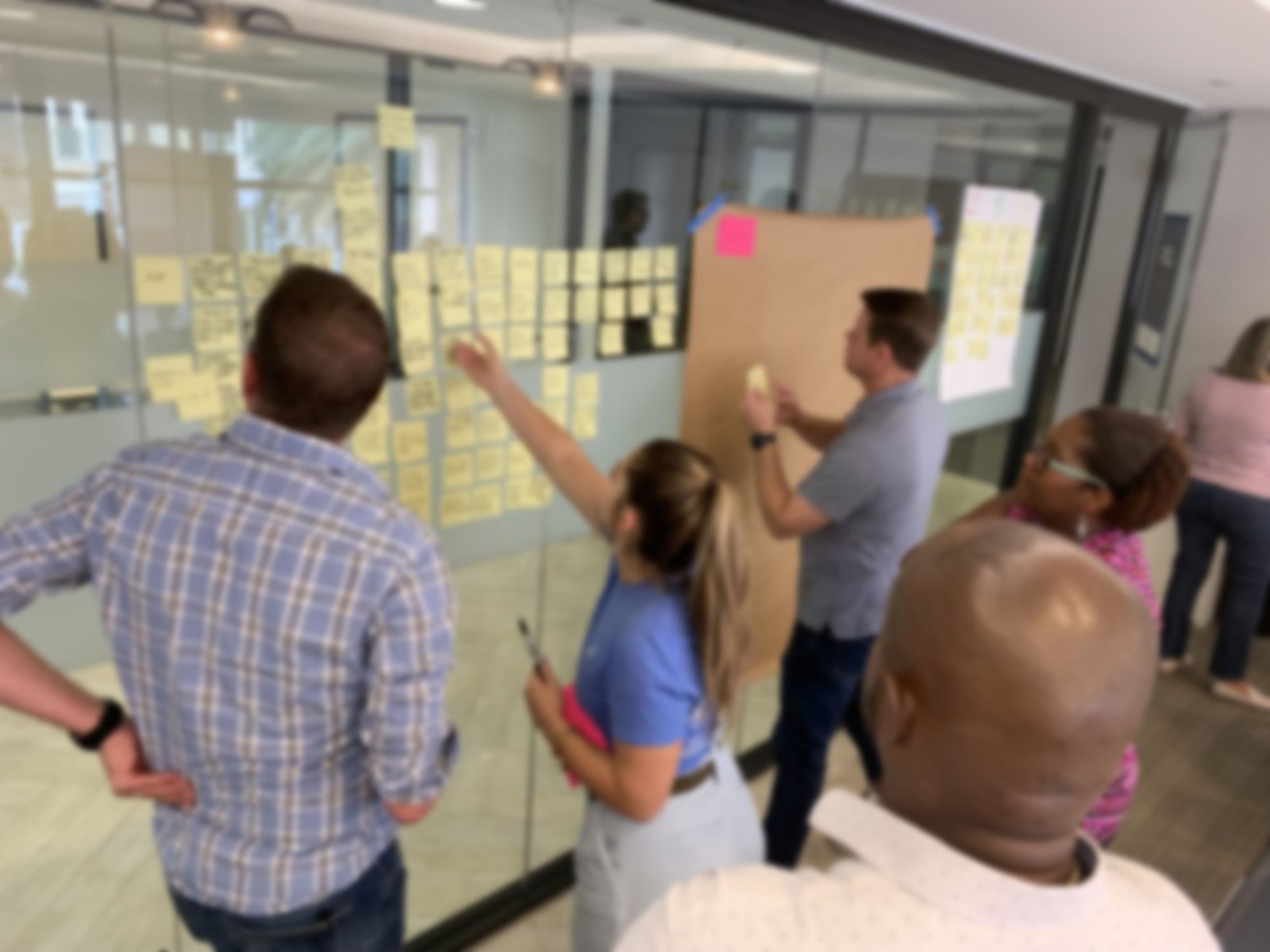 Colleagues gathered around a glass wall covered in sticky notes during a design thinking workshop.