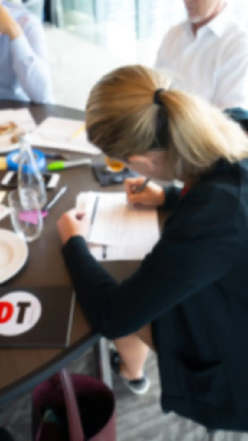 A workshop participant writing on a worksheet at a table during a Contexto session.