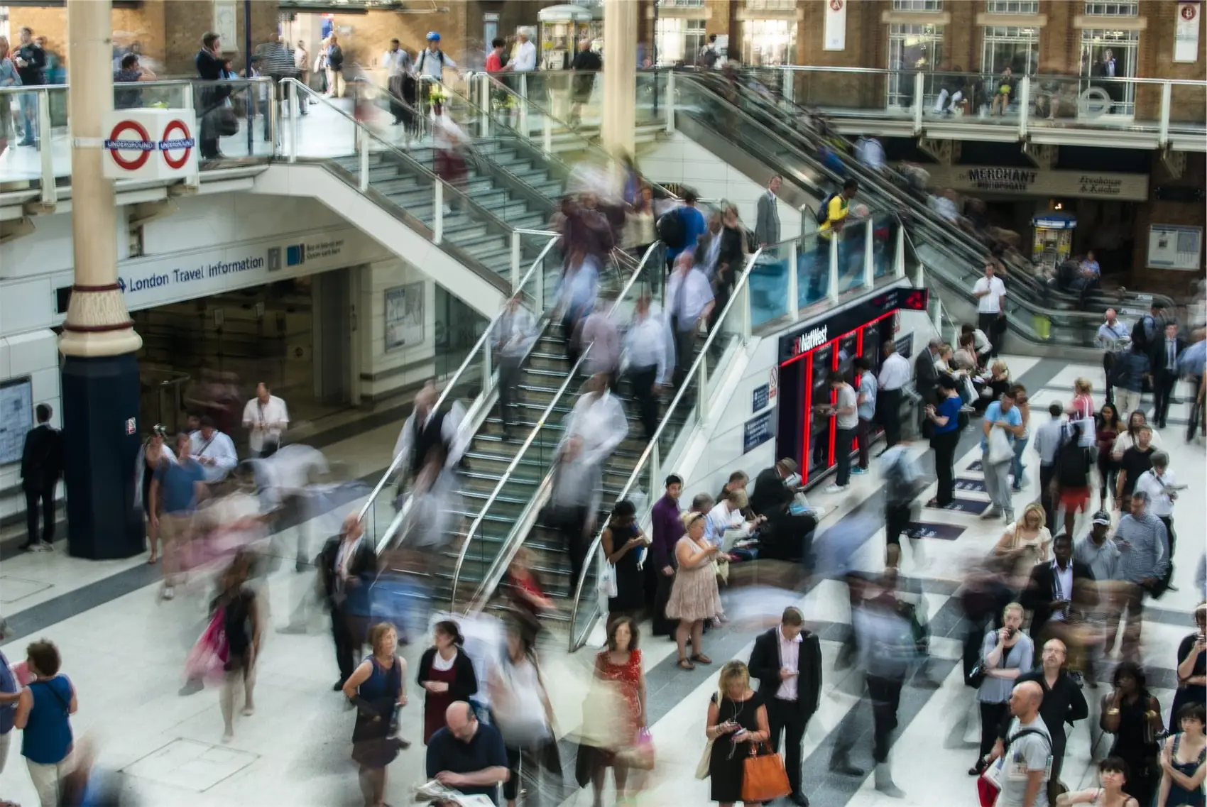 A busy transit hall where hundreds of people move past one another in blurred motion.
