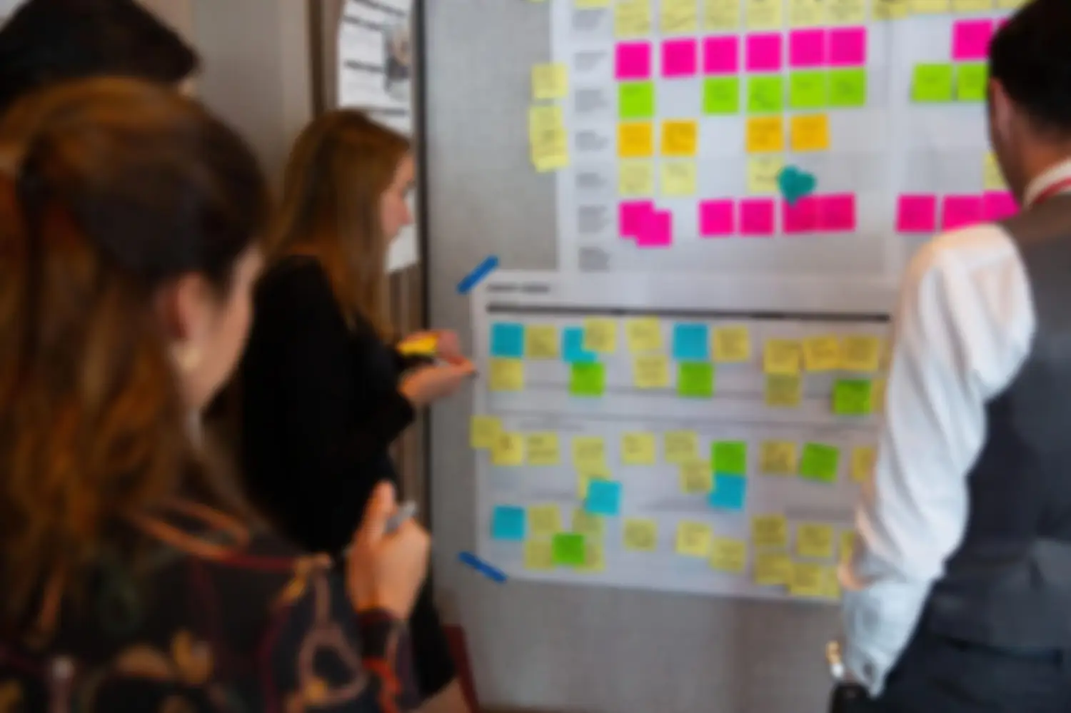 Colleagues clustered at a wall covered in colored notes, mapping a customer journey together.